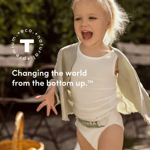 Child wearing a white clothes with a Terra nappy, standing outdoors with text about changing the world.