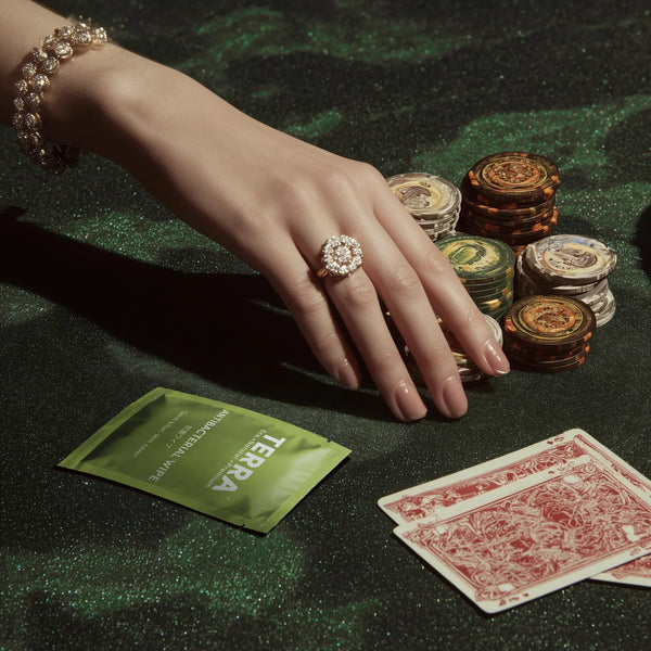 Hand with a ring on a poker table with chips and cards, featuring Terra Antibacterial Wipes.